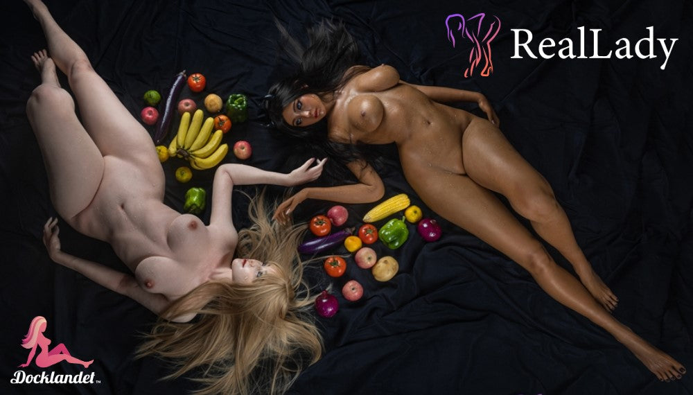 Real Lady - exklusiva silikondockor av högsta kvalitet. På bilden syns en blond och en mörkhårig sexdocka från märket Real Lady. Dockorna är nakna och färgglada frukter är utlagda mellan dockorna. Båda sexdockorna går att köpa hos butiken Docklandet.
